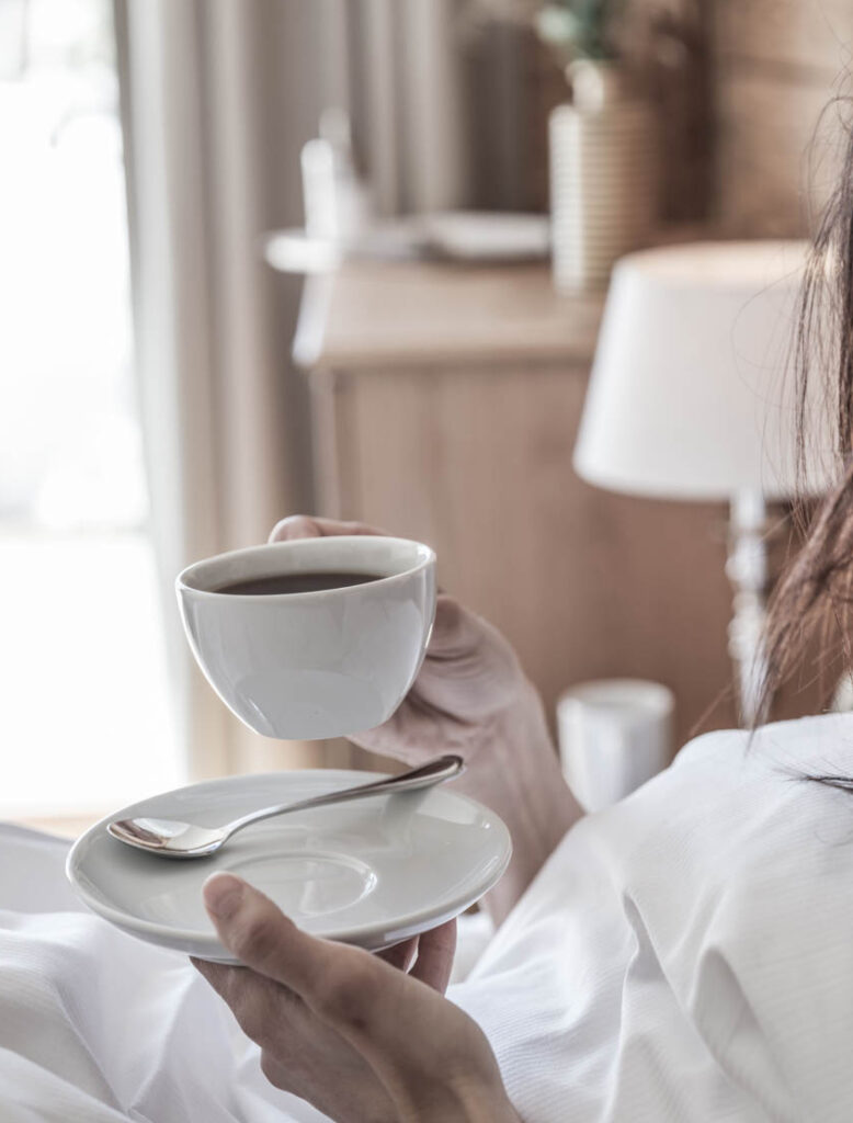 Frau im Bett hält Tasse Kaffe in der Hand | Premium Chalet-Urlaub