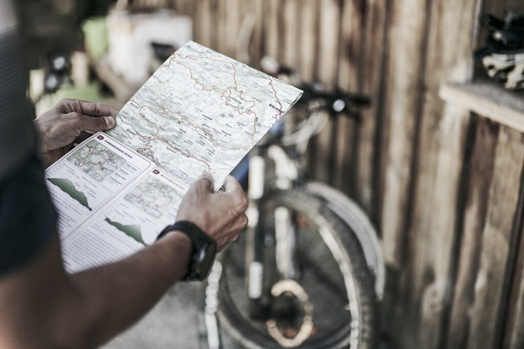 Mountainbiker hält Bikekarte in den Händen, Rad im Hintergrund | Familien Urlaub Bregenzerwald